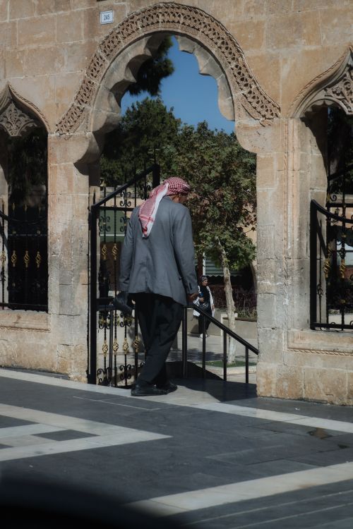 Free Man in traditional attire walks through Middle Eastern stone archway on a sunny day. Stock Photo