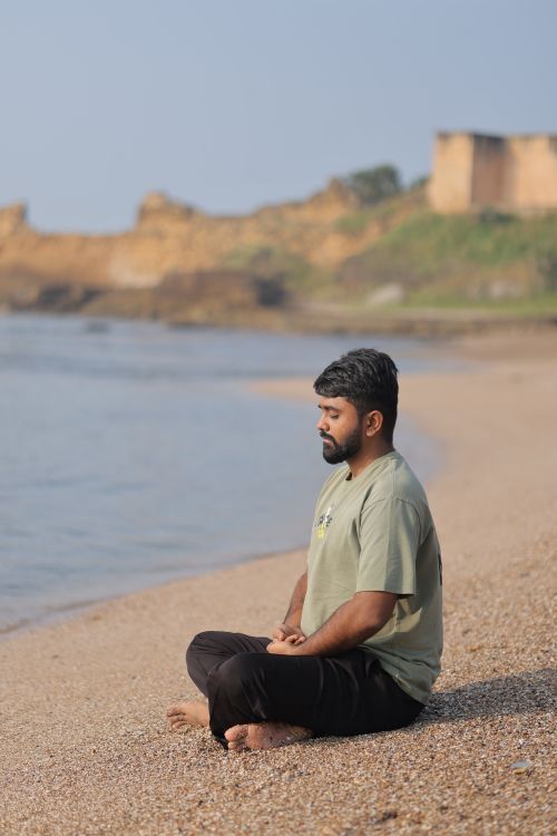 Free A man meditates peacefully on a serene beach with historic ruins in the background. Stock Photo