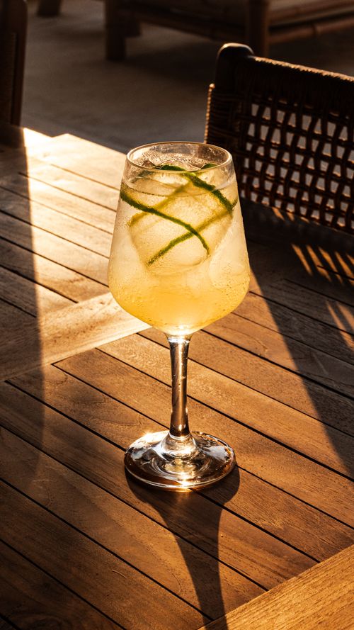 Free Chilled citrus cocktail with lime garnish bathed in warm sunlight on a wooden patio table. Stock Photo