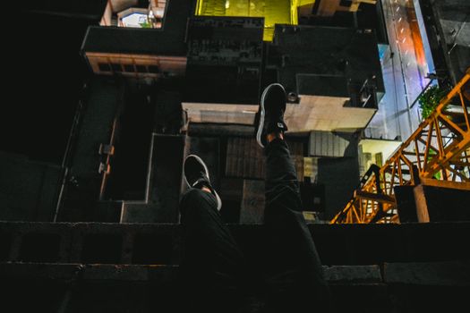 夜晚，大胆的城市屋顶景观中，双腿悬在边缘，展现出一幅城市景象