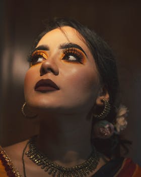 一幅女性特写肖像，她大胆的眼妆和珠宝在柔和的灯光下向上看去