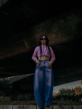 Fashion-forward woman in pink top poses confidently under an urban bridge, showcasing street style.