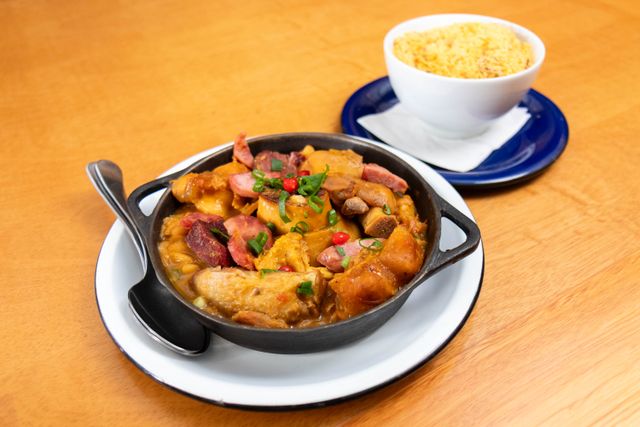 Delicious Brazilian feijoada served in a black pot with a side of rice.