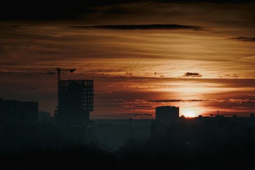 Free A silhouette of a crane and buildings against a vibrant sunset sky in Poznań, Poland. Stock Photo