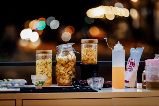 A vibrant display of pickled vegetables in glass jars set at a night market with bokeh lights in the background.