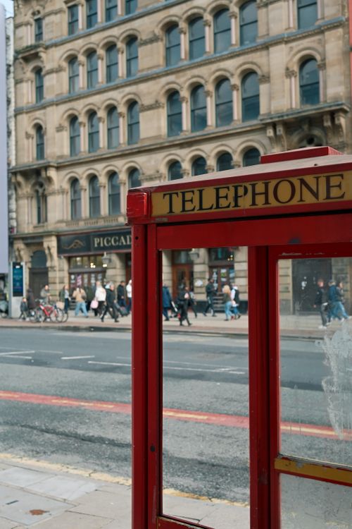 Free Classic red telephone booth on a bustling street with historic architecture in the background. Stock Photo