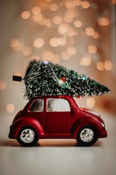 A red toy car carries a Christmas tree, set against a warm bokeh background, celebrating the festive season. by Kristina Paukshtite