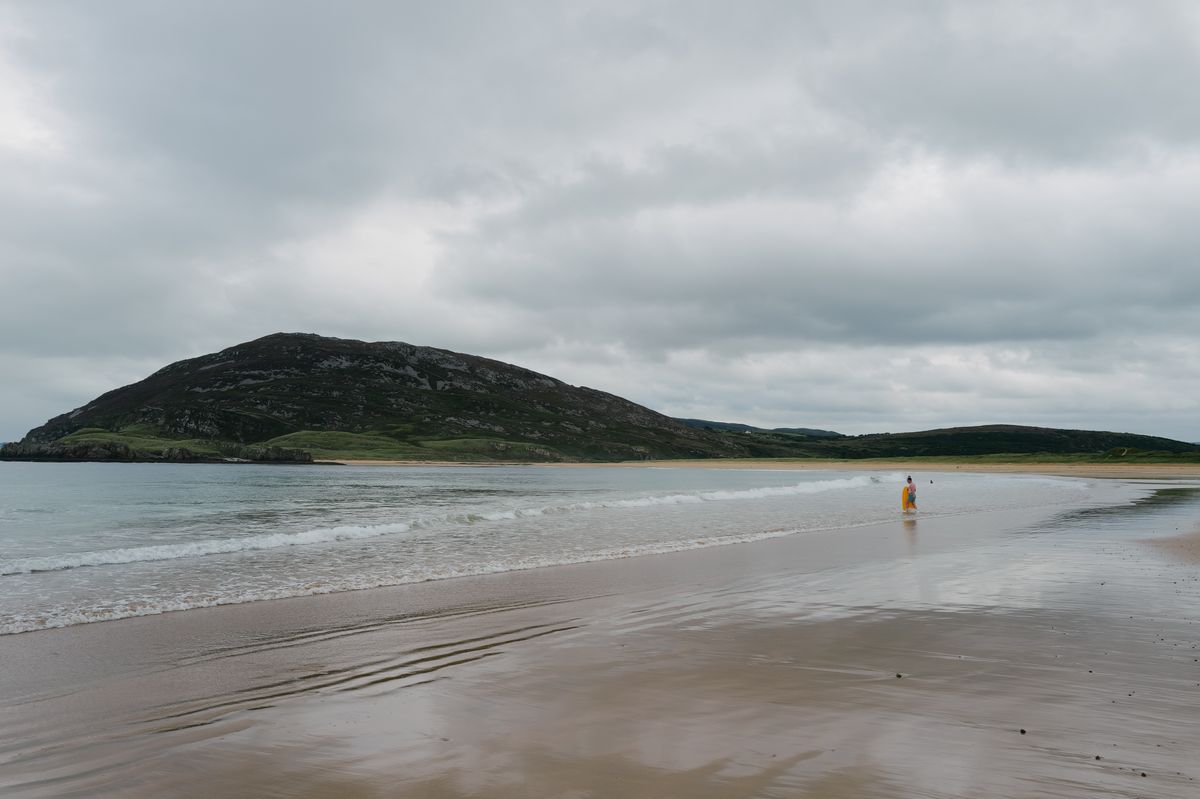 Plaja cu munte in fundal si un drumet solitar