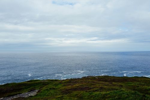 Free Tranquil view of the ocean from a grassy clifftop under a cloudy sky. Stock Photo