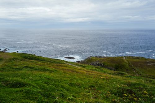 Free A tranquil view of a lush coastal landscape meeting the expansive ocean under a cloudy sky. Stock Photo
