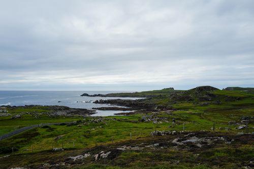 Free A serene coastal landscape featuring rocky shores and lush green hills under a cloudy sky. Stock Photo