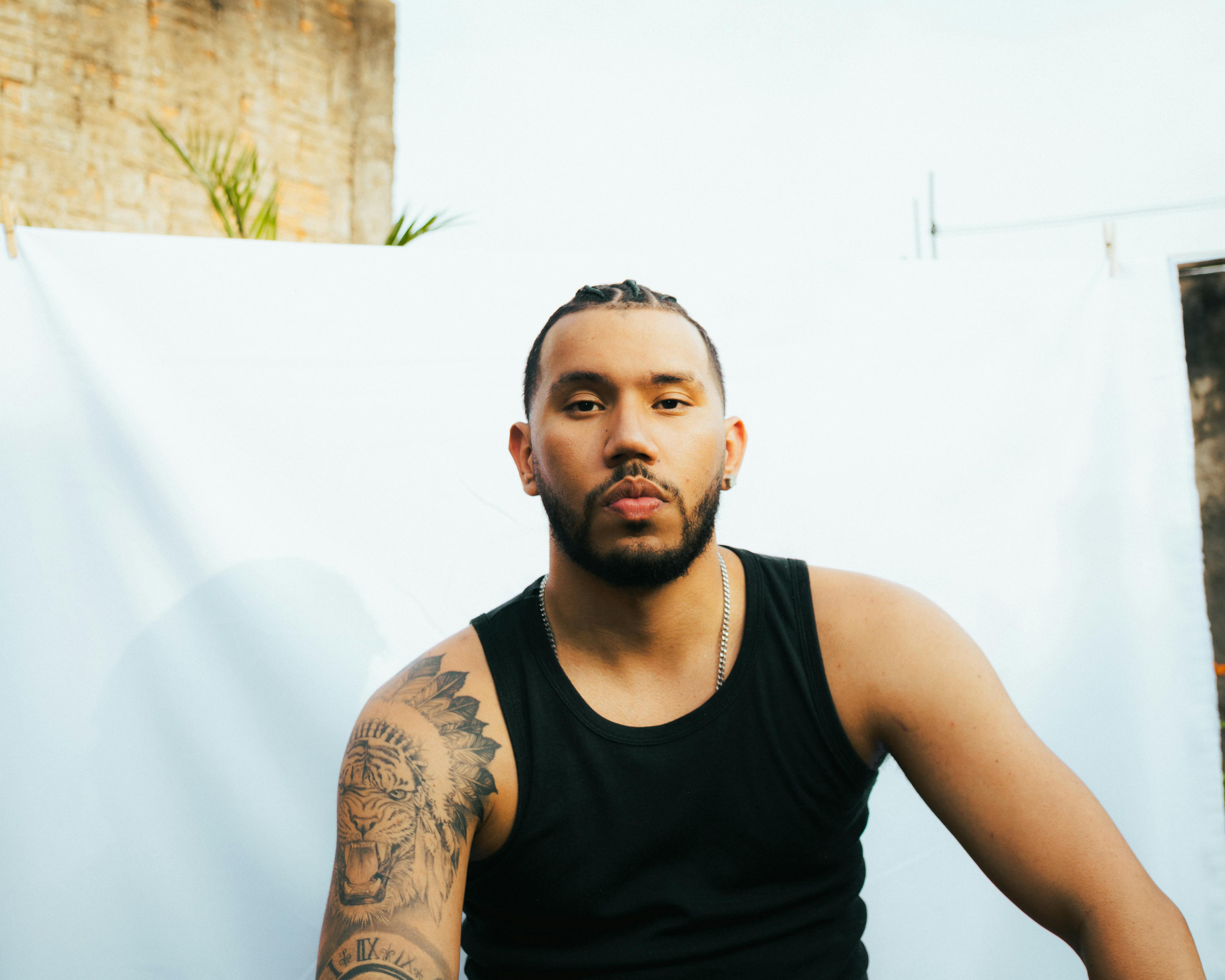 A young tattooed man with braids poses outdoors in São Paulo, Brazil.