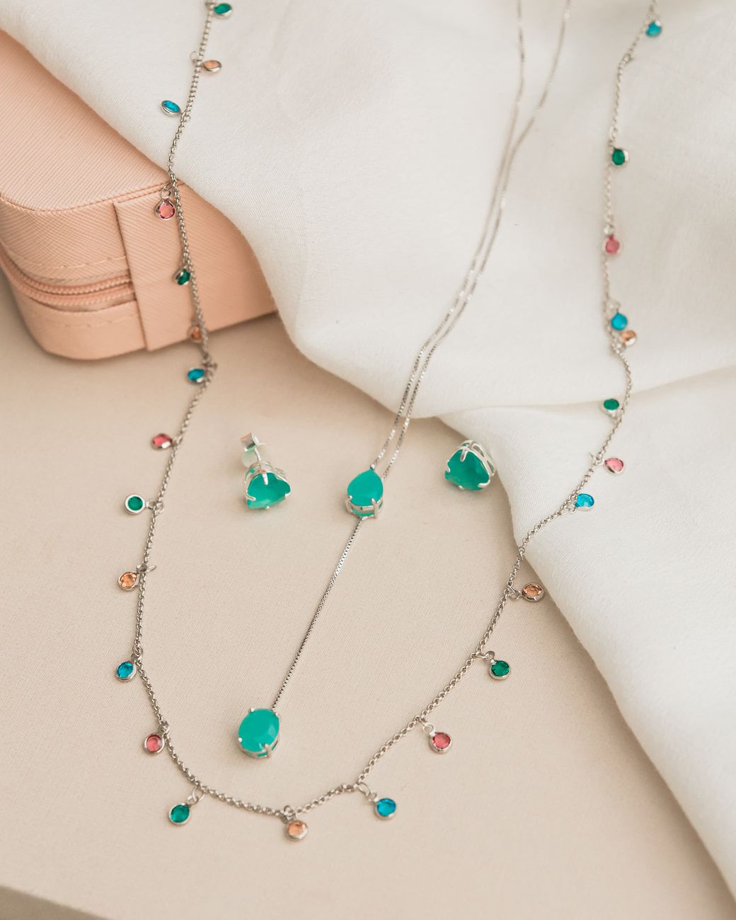 Conjunto de colar e brincos com pedras preciosas lindamente desenhado, com pedras coloridas dispostas em um tecido macio.