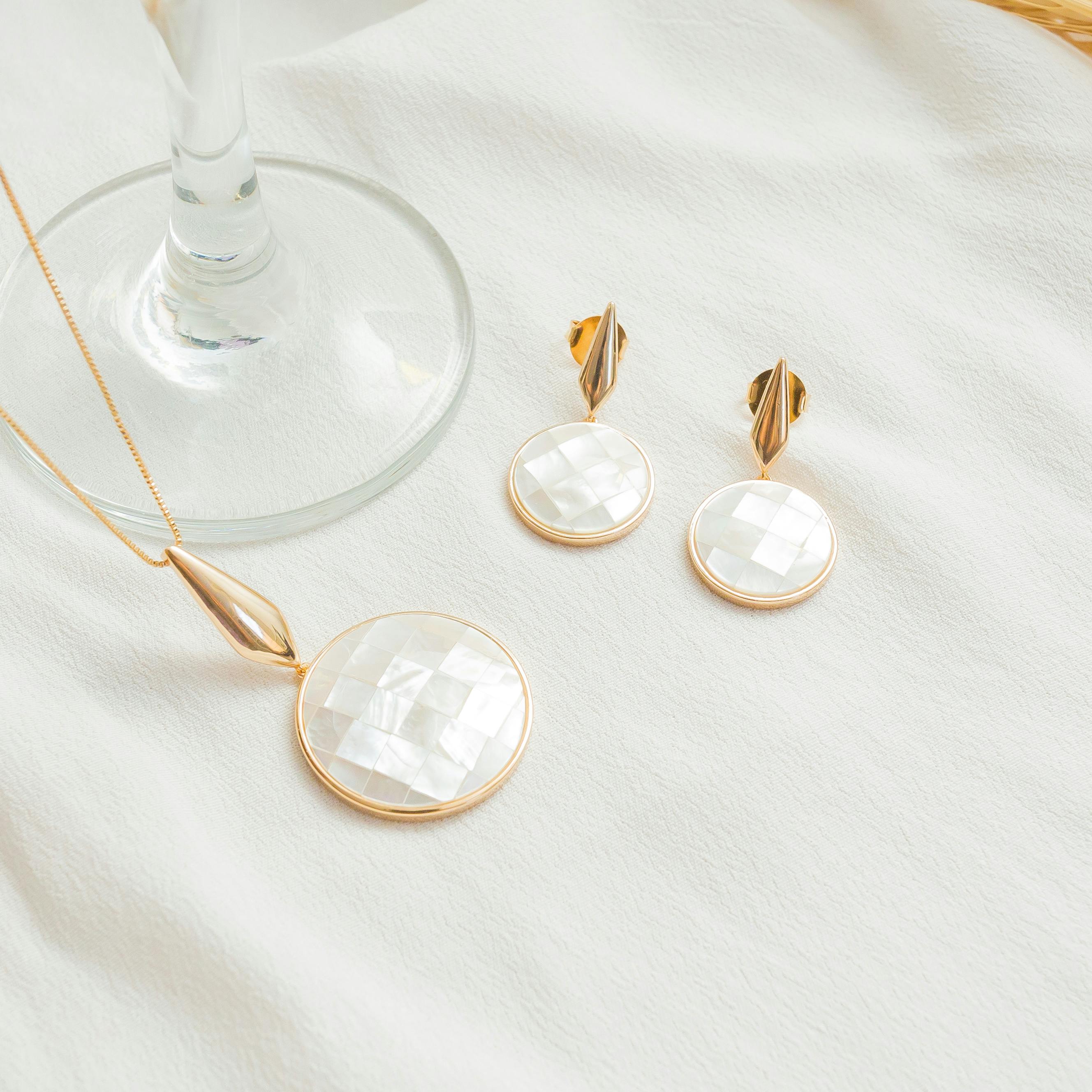 A stylish set of mother-of-pearl necklace and earrings displayed on white fabric.