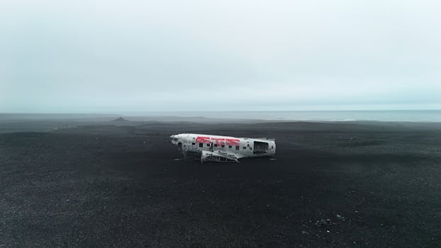 Drone view of a crashed plane on the black sands of Iceland, evoking a moody, dark atmosphere.
