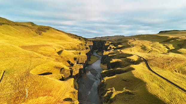 A stunning aerial view of Fjadrargljufur Canyon in Iceland, showcasing golden landscapes and winding river.