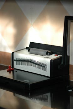 Close-up of a metal binding machine reflecting on a glossy surface, indoors.