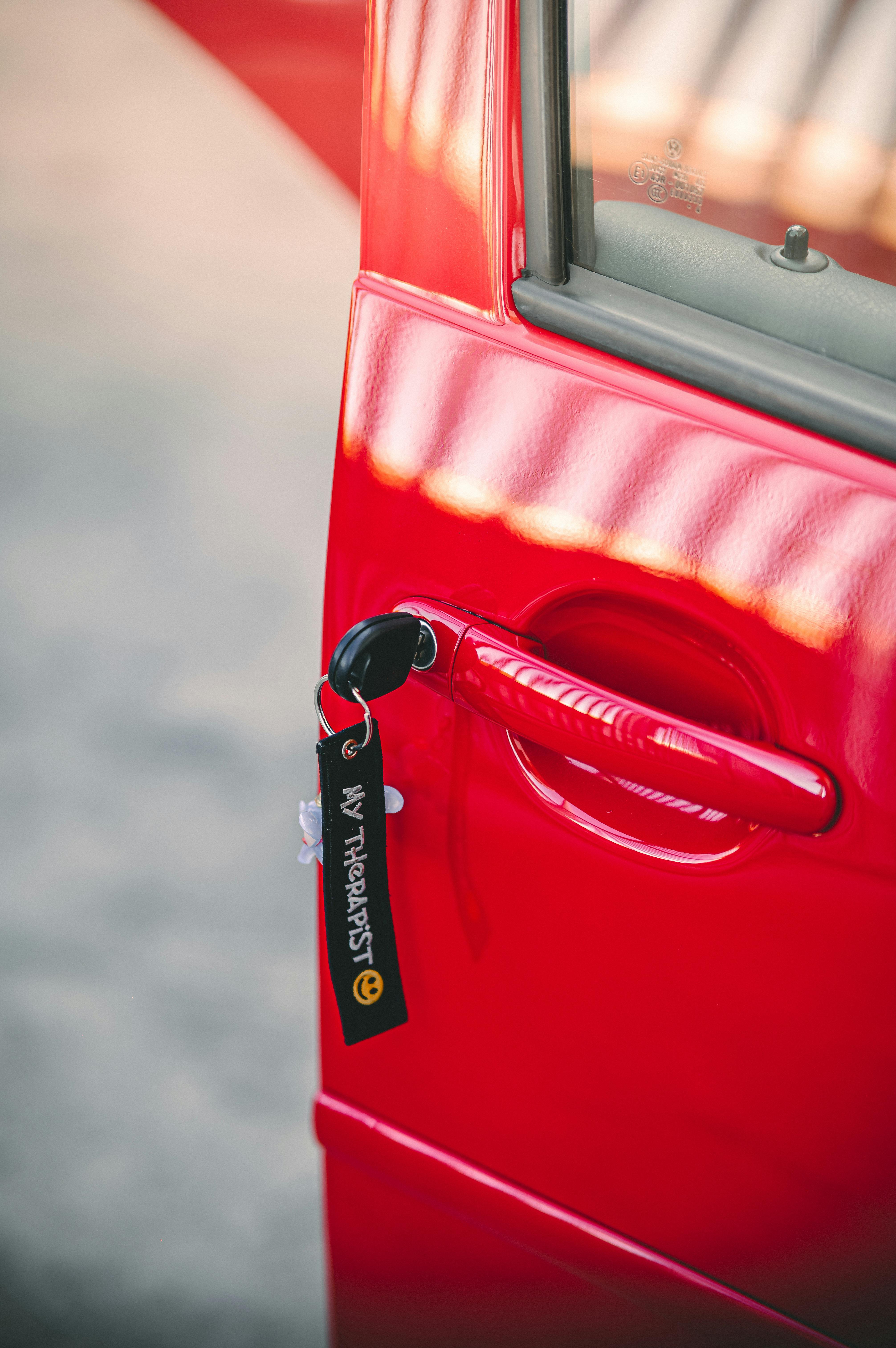 Close-up of a red car door with 'My Therapist' keychain in sunlight.