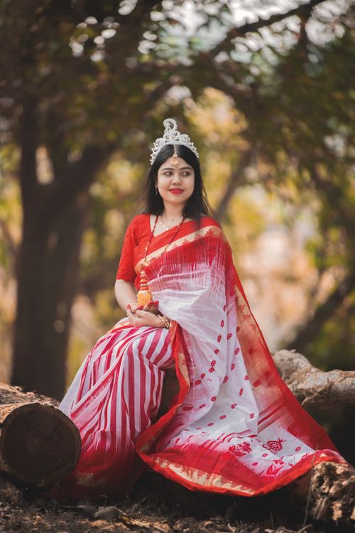 Free An elegant woman poses outdoors wearing a red and white saree, embodying cultural grace. Stock Photo