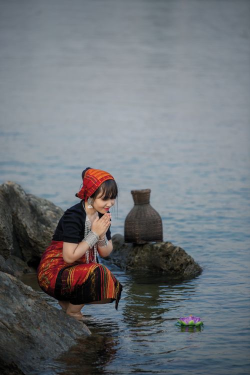 Free Woman in traditional attire by a river, engaging in cultural ritual with basket. Stock Photo