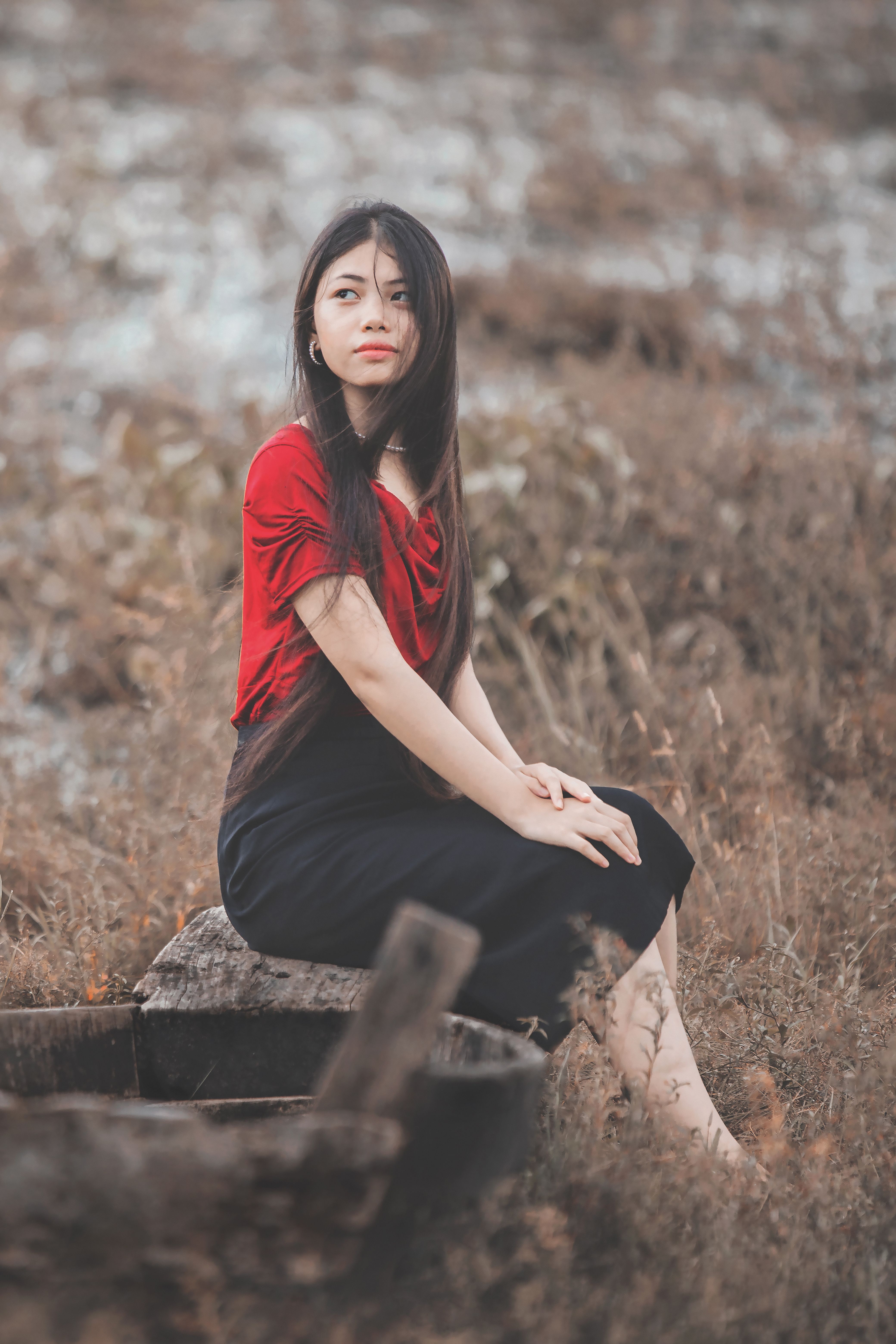 A young woman in a red top sitting in a scenic rustic outdoor location. Calm and serene atmosphere.