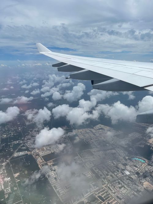 Free Aerial view from airplane window showing wing over clouds and cityscape below. Stock Photo