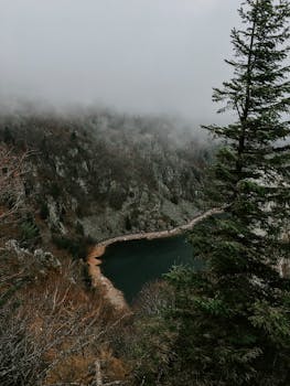 树木和云层环绕着朦胧的山景与宁静的湖泊