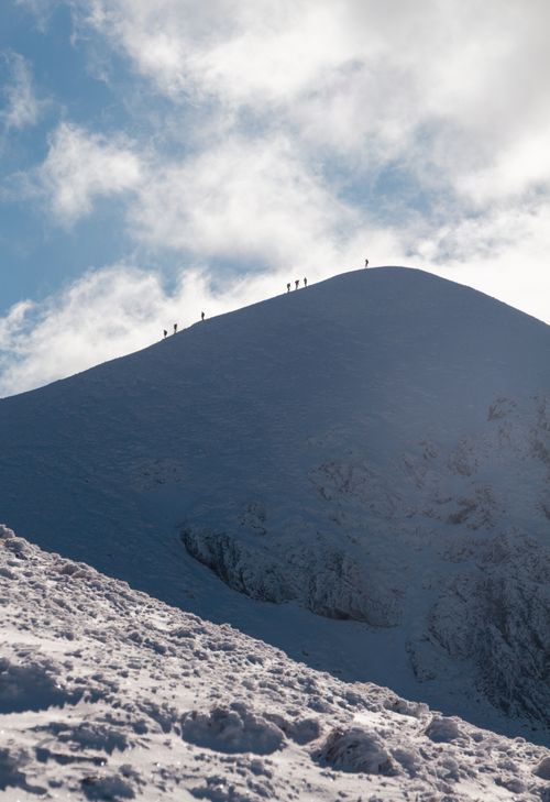 Free A group of climbers ascends a snow-covered mountain peak under a bright blue sky. Stock Photo