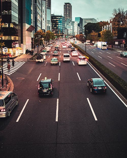 Avenue with cars and vans moving fast past high rise buildings in modern Japanese city in evening