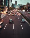 Avenue with cars and vans moving fast past high rise buildings in modern Japanese city in evening