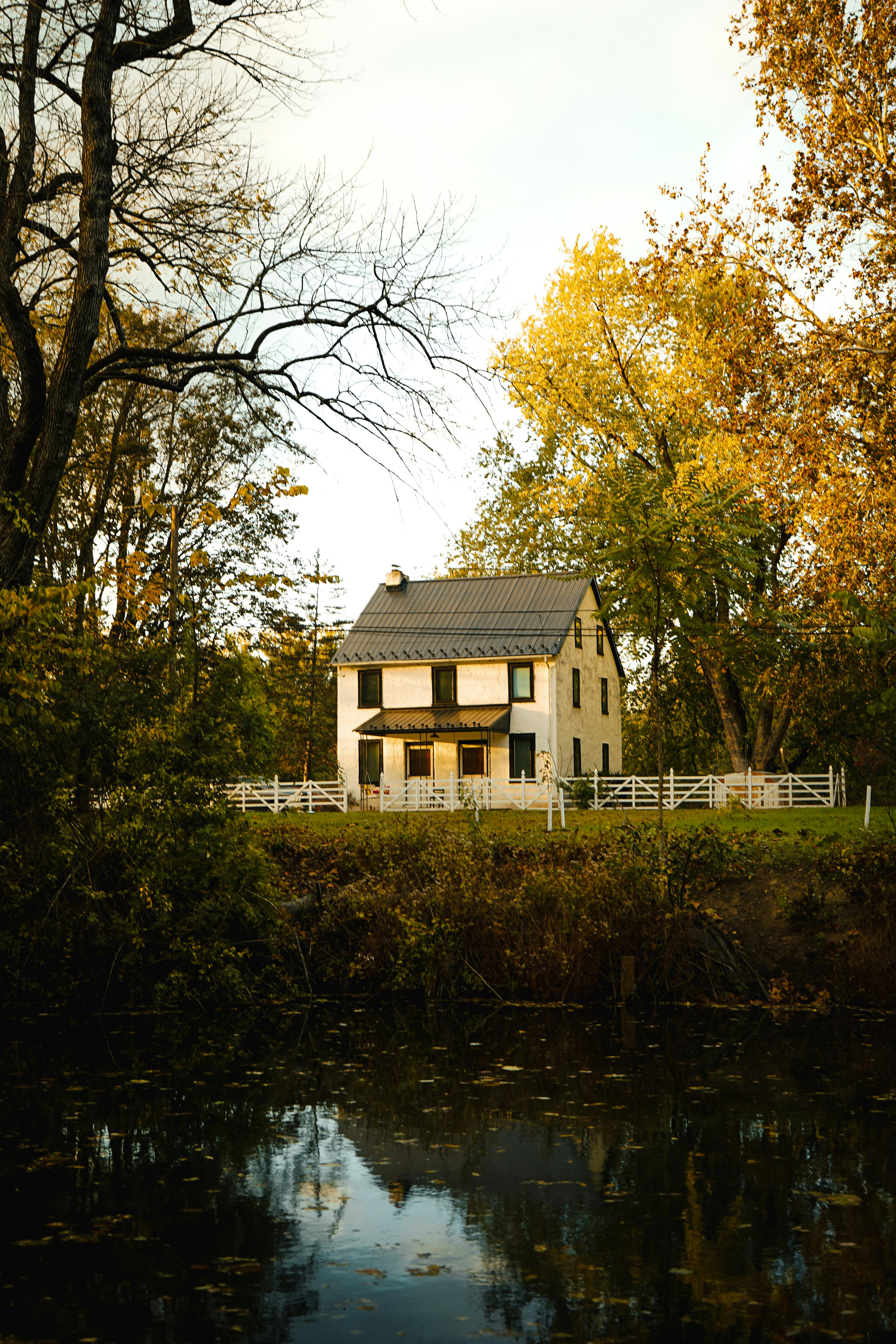 Idyllic cottage beside a calm lake surrounded by vibrant autumn foliage.