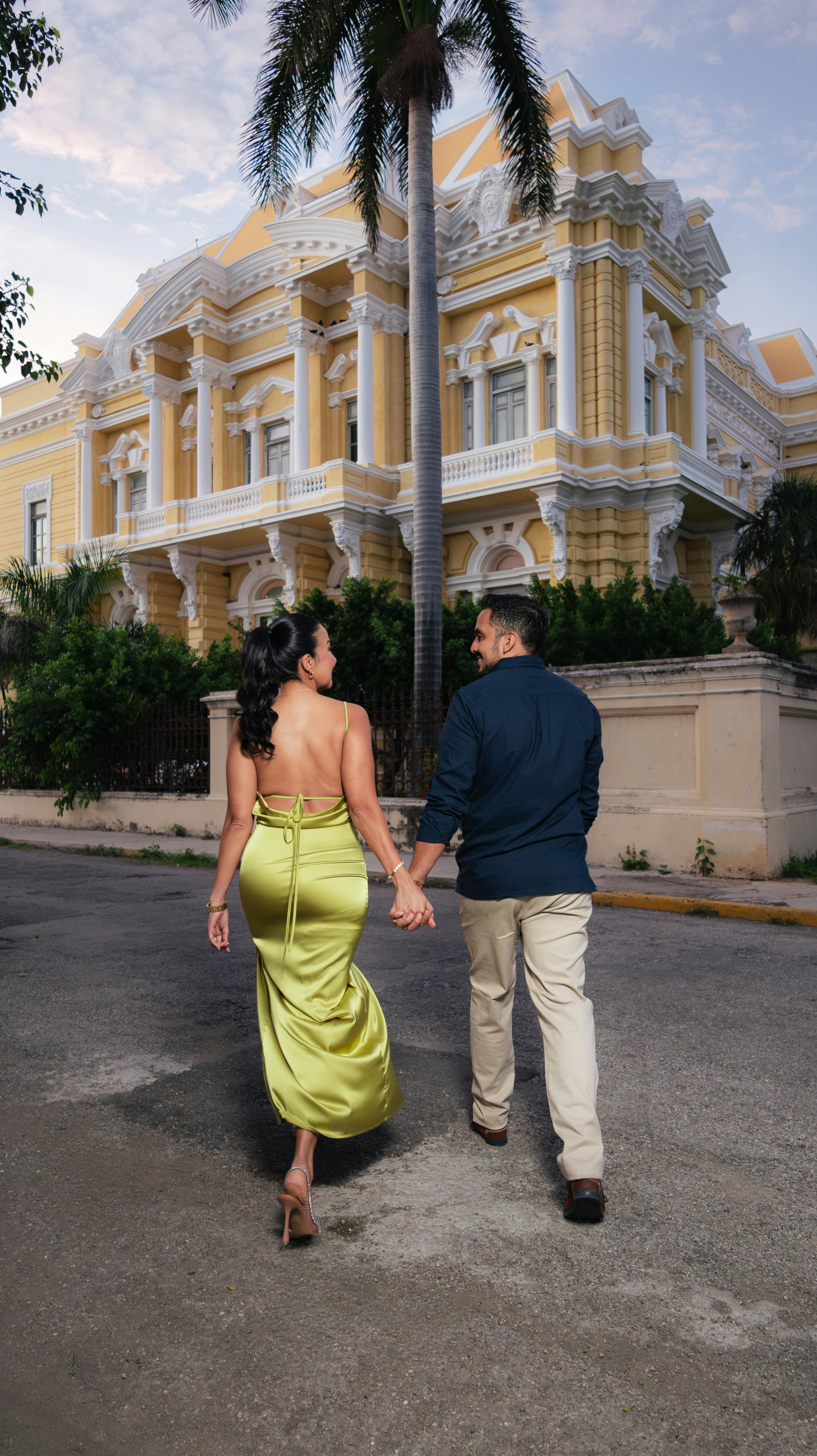 A couple walks hand in hand past a grand historic mansion on a serene evening.