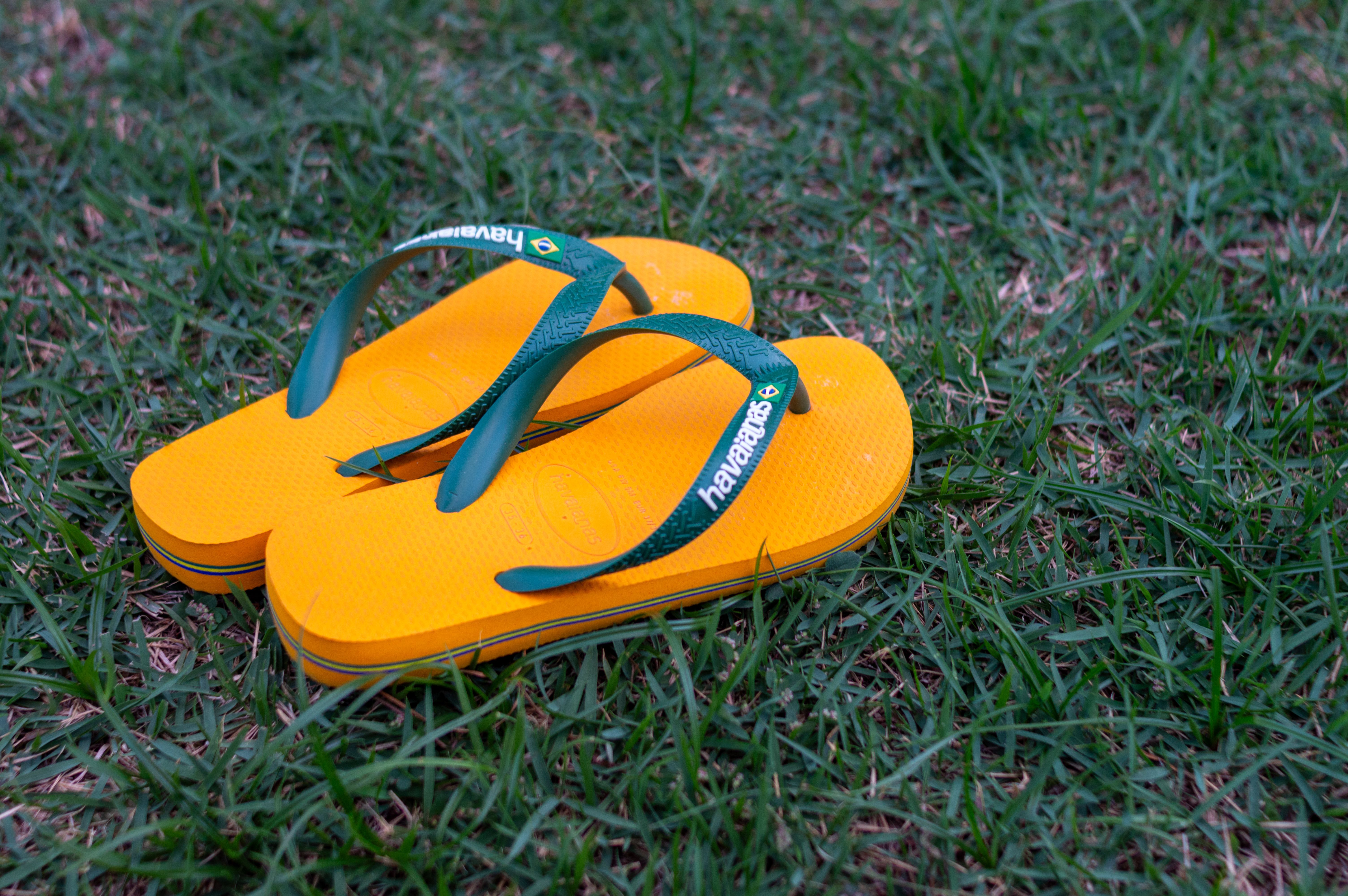 Chinelo de borracha amarelo em um campo de grama, simbolizando lazer ou atividades ao ar livre.