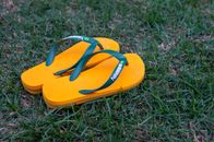 Bright yellow flip flops with green straps resting on lush green grass, creating a summery feel.