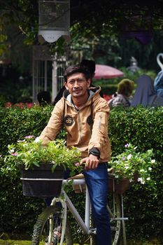 A man stands beside a bicycle with flowers in a lush outdoor park setting. - Fotografer Sidoarjo