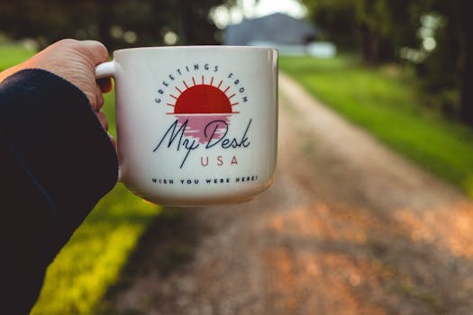 Person holding a coffee mug with scenic view of a country road, conveying warmth and relaxation.