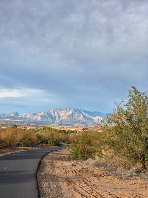 Free Desert landscape featuring a winding road leading to majestic mountains under cloudy skies. Stock Photo