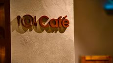 Close-up of a stylish café sign with warm lighting casting shadows on a textured wall.