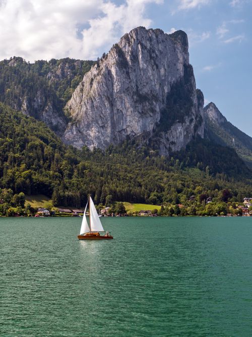 Free A serene sailboat glides on a lake with stunning mountain views, ideal for travel and nature themes. Stock Photo