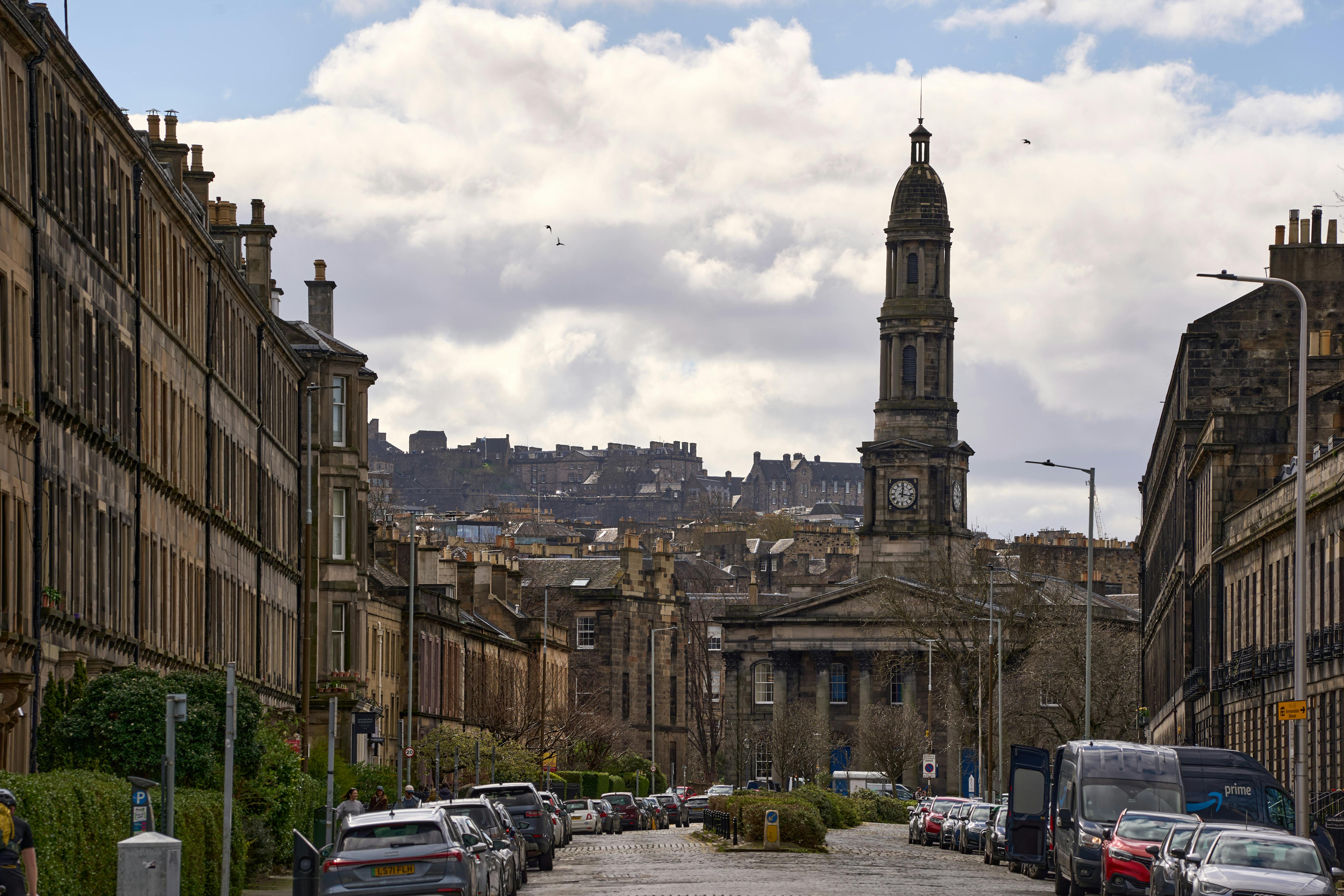 View of a historic Edinburgh street with beautiful architecture and a prominent clock tower in spring.