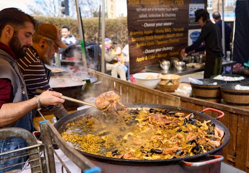 Street food vendors preparing sizzling seafood paella at an outdoor market in spring.