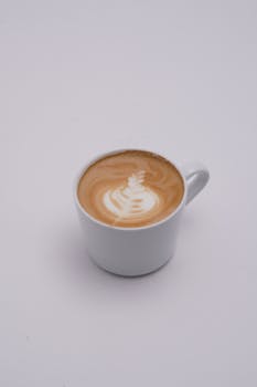 A minimalist image of a latte with intricate art in a white mug on a plain background.