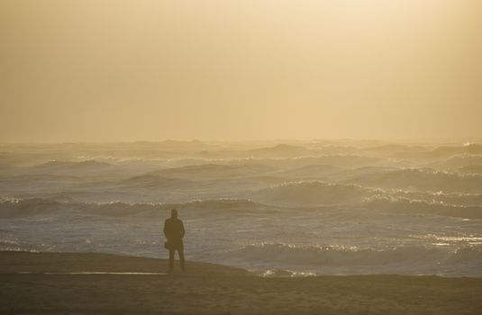 A lone figure stands by the ocean at sunrise, capturing a serene and contemplative moment.