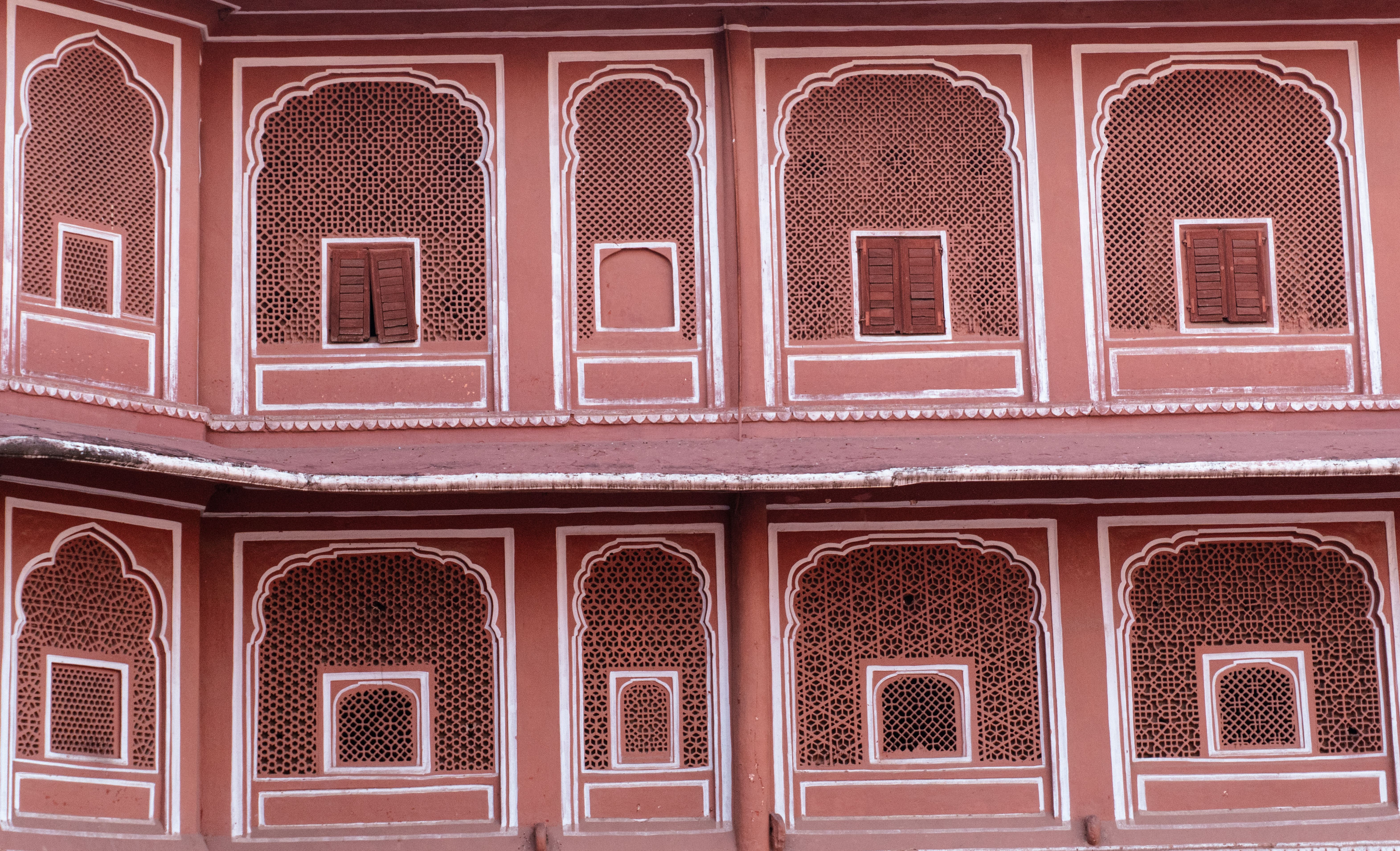 Close-up of intricate red sandstone lattice jharokha windows showing traditional Jaipur stone craftsmanship in deep warm red