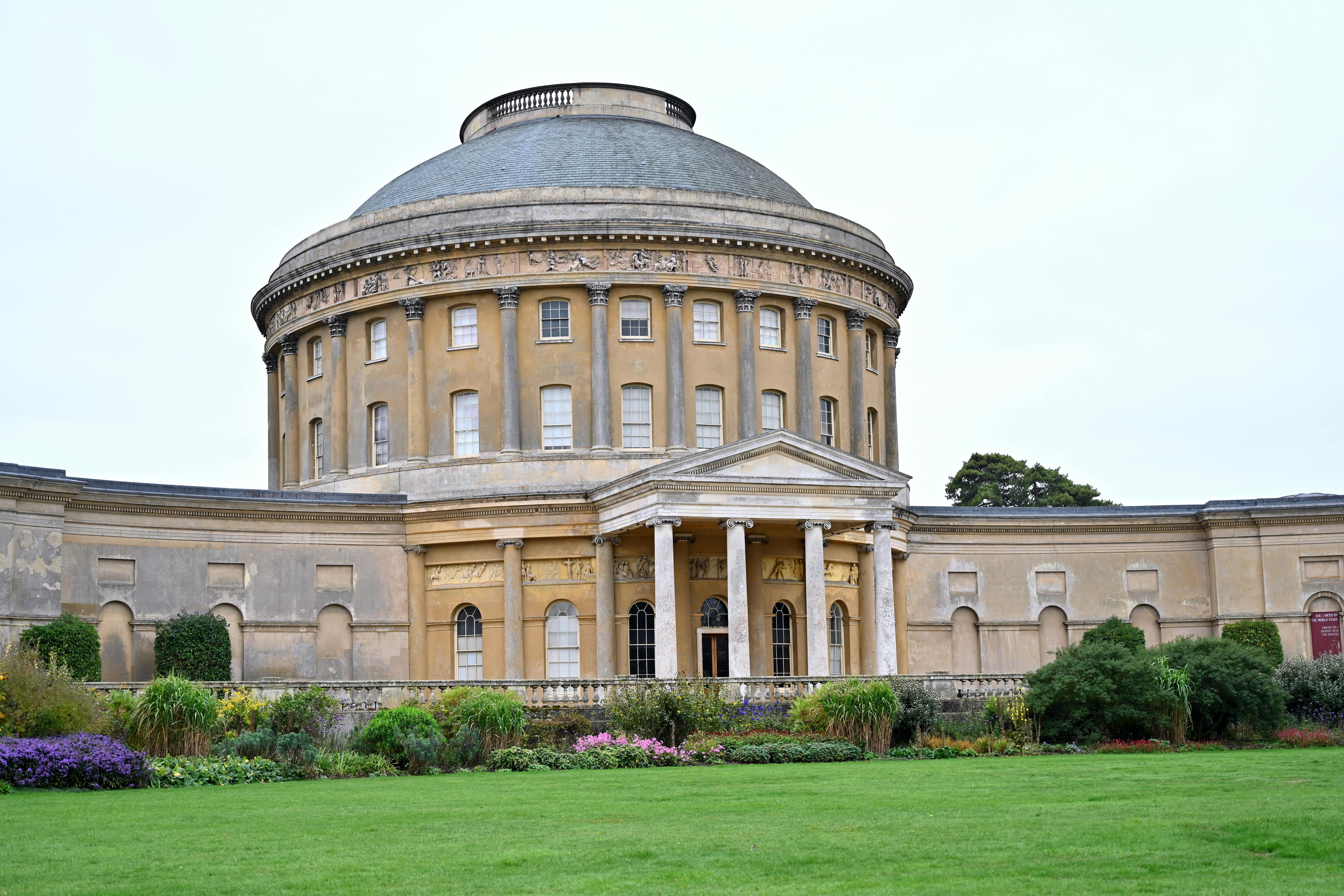 Elegant historic rotunda with columns and lush garden in foreground, showcasing classic architectural style.