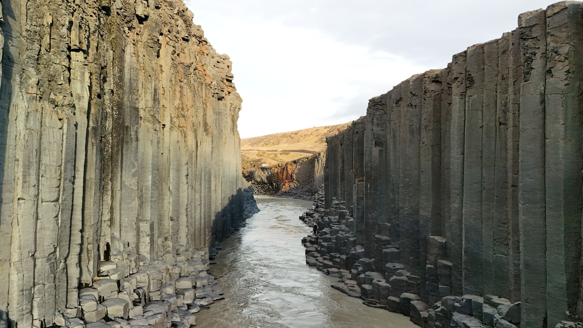 Towering hexagonal basalt columns framing a turquoise river inside Studlagil Canyon