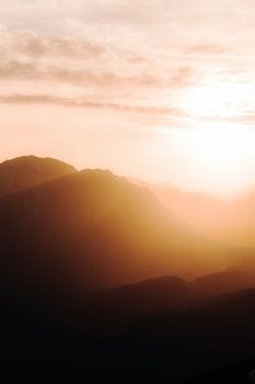 Beautiful sunset over a misty Austrian mountain range with warm orange hues.