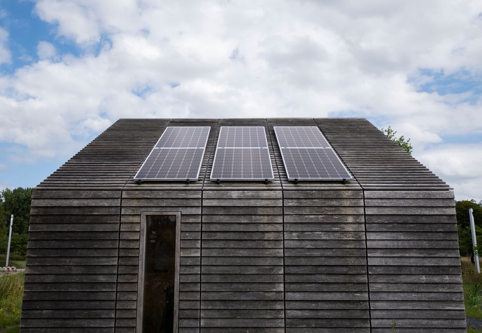 Wooden house with solar panels under a cloudy sky, promoting sustainable energy.