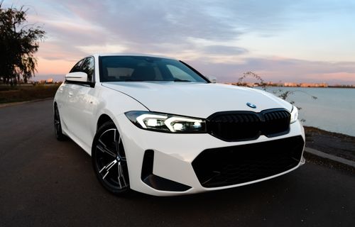 Free Elegant white sedan parked by a lake during sunset, with city skyline in the background. Stock Photo