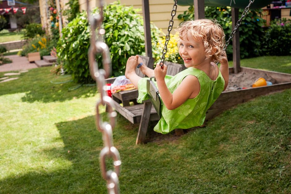 Photo by Ian Taylor on Pexels Joyful child swinging in a backyard garden on a sunny day, capturing summer fun.